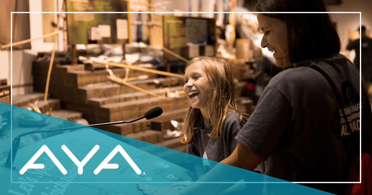 Two people smile and listen to Chickasaw history at an interactive museum exhibit.